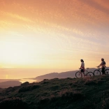 Dau berson gyda beic mynydd yn edrych ar yr haul yn machlyd yn aber afon Mawddach eastuary.