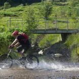 Beiciwr yn torri trwy afon yng Ngheredigion