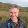 A smiling grey haired man on a hillside.