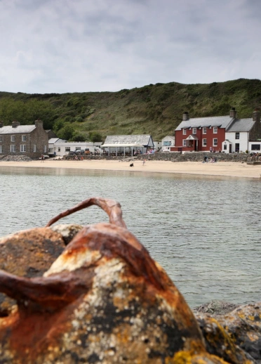 Golygfa o gildraeth creigiog ar arfordir gydag adeiladau yn y cefndir.