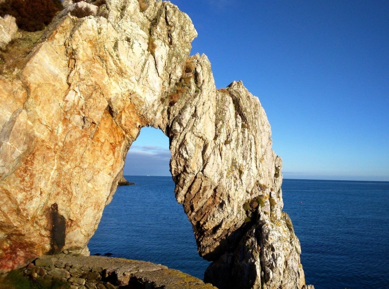 bwa naturiol mewn clogwyn gyda môr glas y tu ôl iddo 