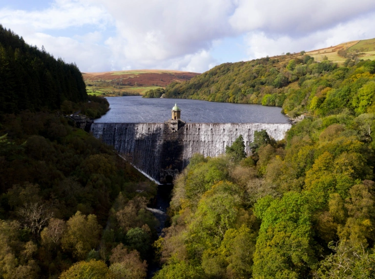  Argae yn dal yr afon yn ôl wedi'i fframio mewn coed yn troi lliw yn yr hydref.