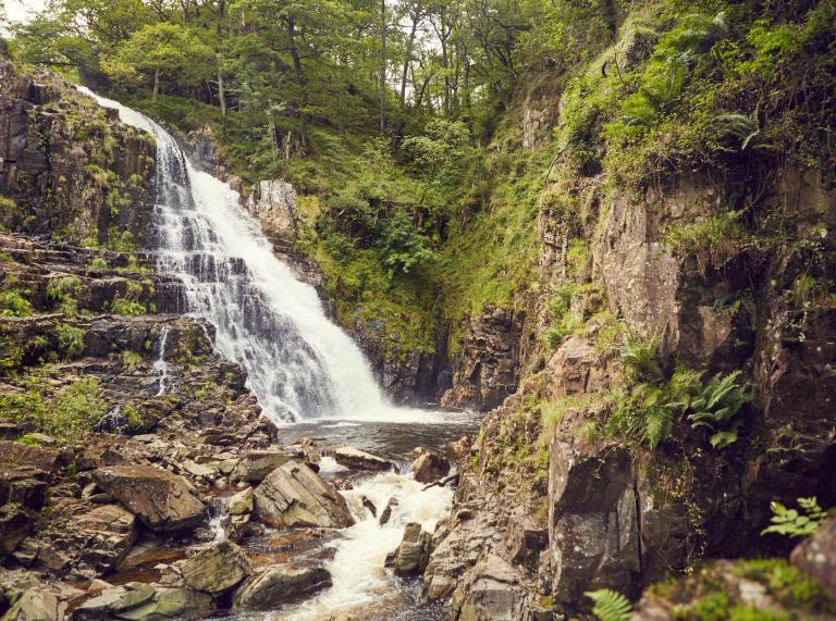 Rhaeadr â chreigiau a gwyrddni o’i amgylch.