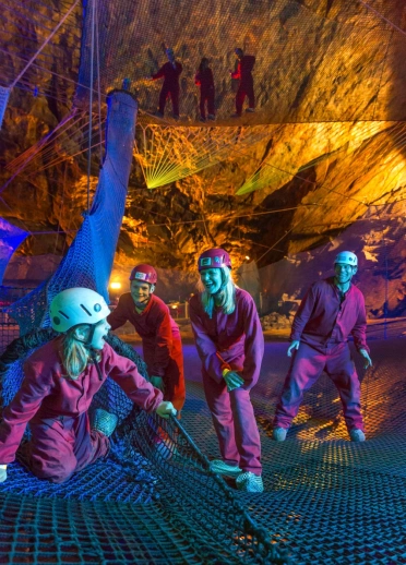 Grŵp o bobl ar rwydi’r parc trampolîn tanddaearol Bounce Below yn Zip World Slate Caverns.