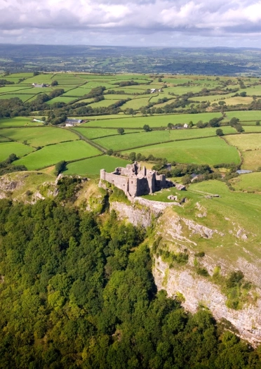 Golygfa o’r awyr o gastell ar fryn yng nghanol caeau gwyrdd.