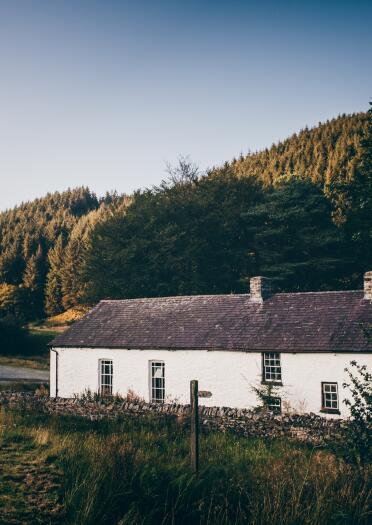 Tu allan i gapel gwyn gyda choed a gwyrddi o'i amgylch.