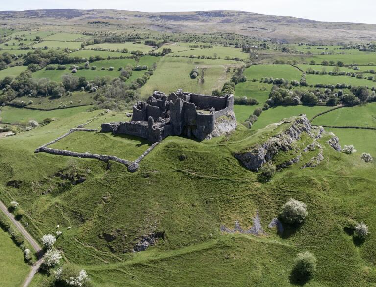 Llun oddi fry o adfail castell yng nghanol cefn gwlad gwyrdd.