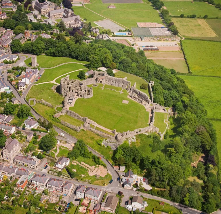 Llun o'r awyr o gastell Dinbych. Mae tai a bryniau gwyrdd o'i gwmpas. 