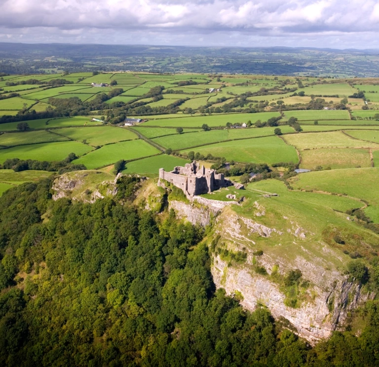 Golygfa o’r awyr o gastell ar fryn yng nghanol caeau gwyrdd.