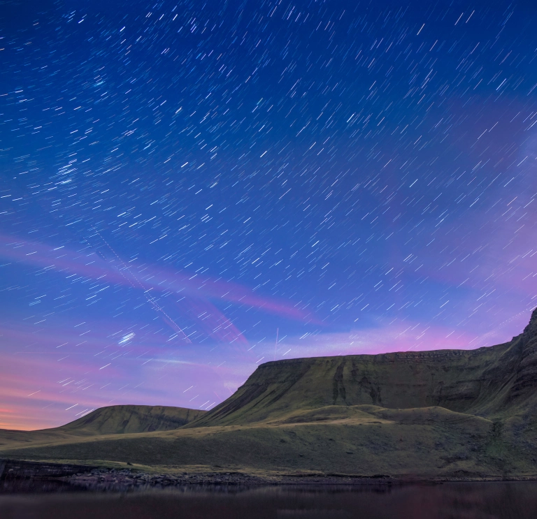 Llun o olion y sêr yn yr awyr, uwchben y llyn gyda mynyddoedd yn y cefndir