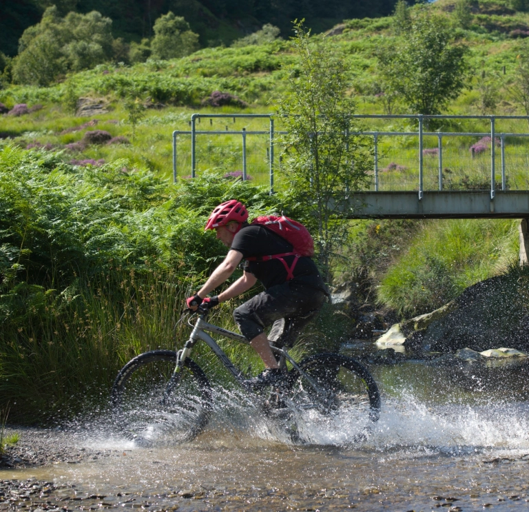 Beiciwr yn torri trwy afon yng Ngheredigion