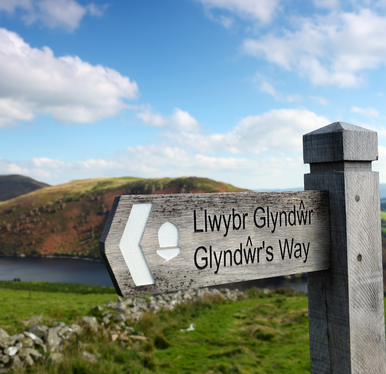 Arwydd Llwybr Glyndŵr gyda Llyn Clywedog a bryniau yn y cefndir  