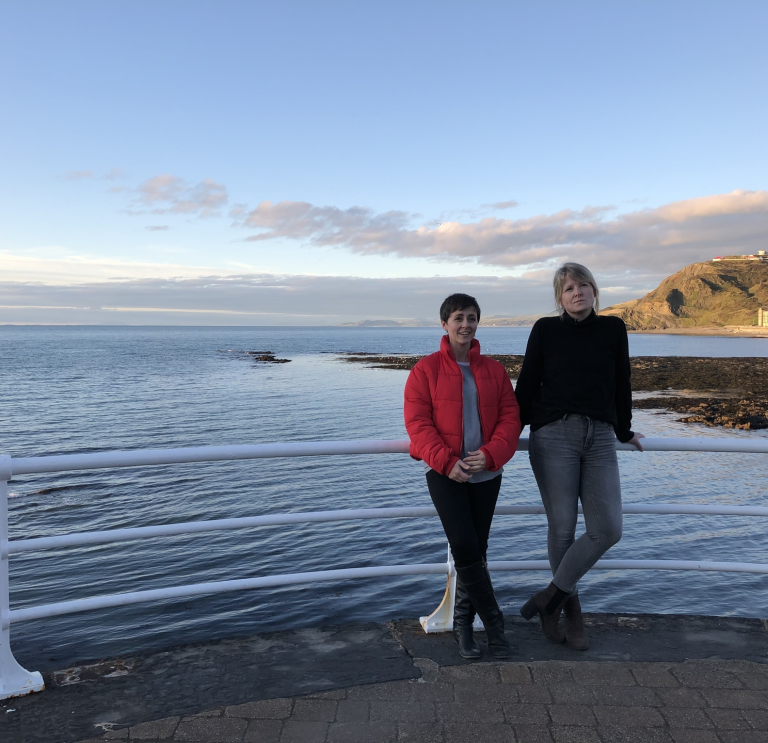 Two women in front of the sea with Constitution Hill in the background.