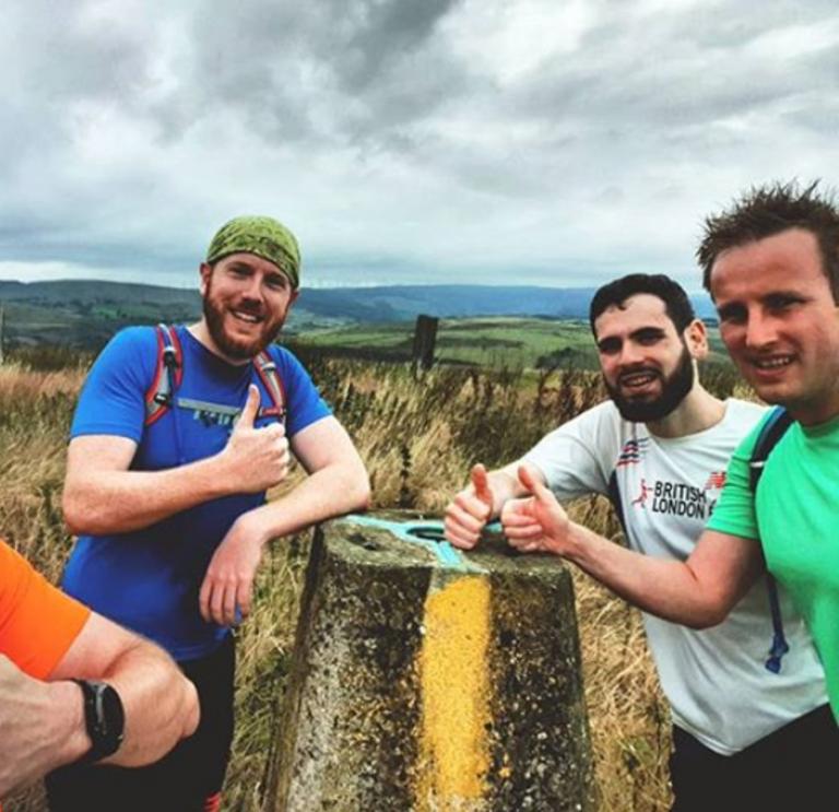 Four men doing a thumbs up sign at stone marker in Llanwono forestry  after trail running.