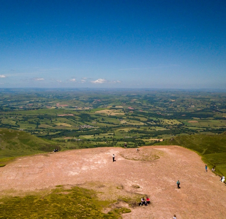  Golygfa o'r awyr o'r gwastadeddau gwyrdd islaw o ben Pen y Fan gydag awyr las.