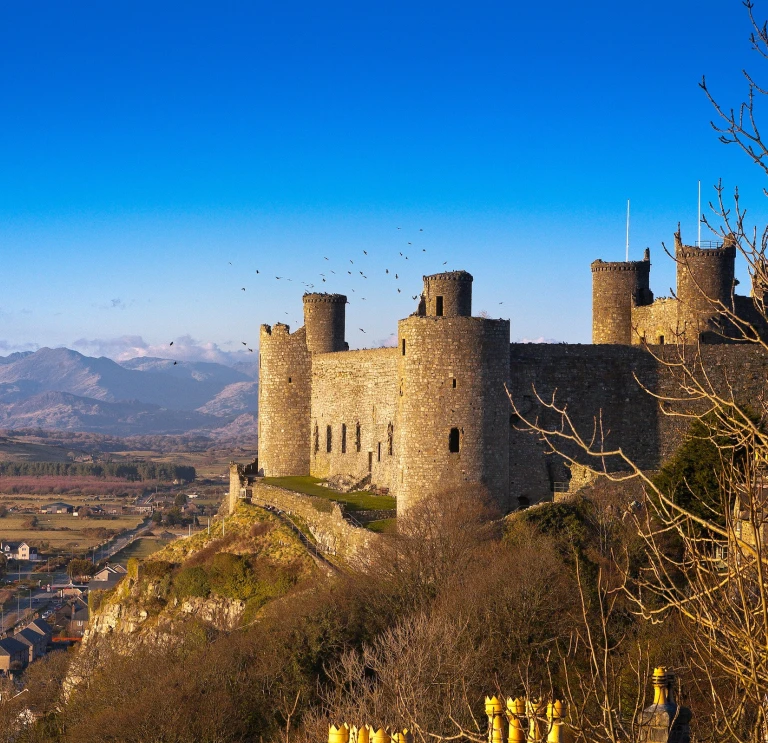 Castell ar fryn wedi’i amgylchynu gan gefn gwlad gyda mynyddoedd yn y cefndir