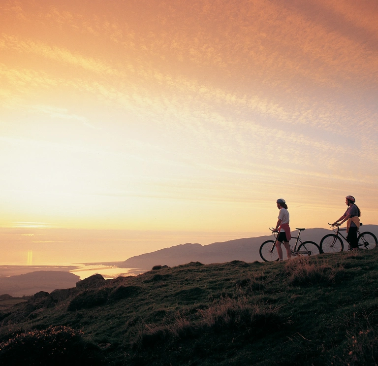 Dau berson gyda beic mynydd yn edrych ar yr haul yn machlyd yn  aber afon Mawddach eastuary.