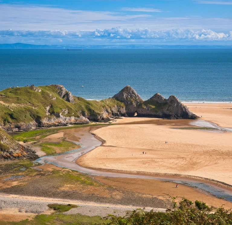 Llanw allan ym Mae'r Tri Chlogwyn gyda thraeth tywodlyd.