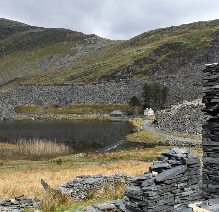 Llyn gyda mynyddoedd o'i amgylch a wal lechi. 