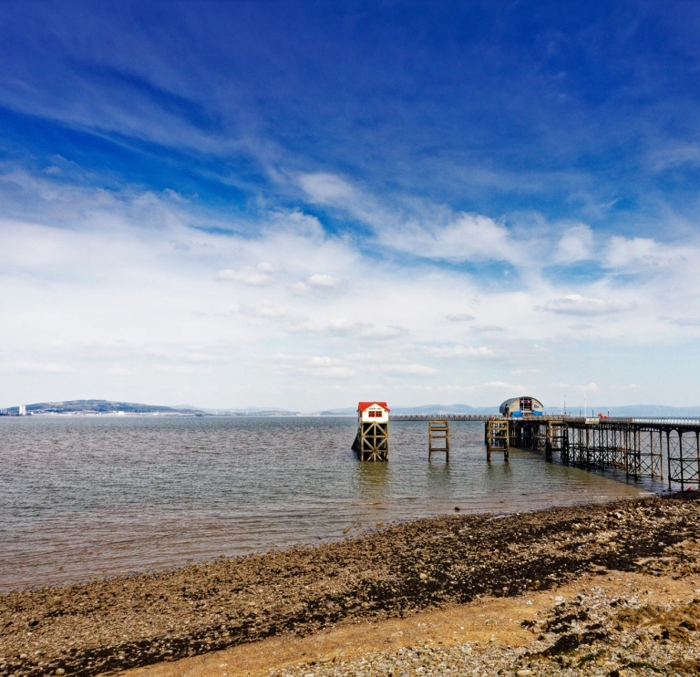 Pier yn mynd allan i'r môr gydag awyr las yn gefndir. 