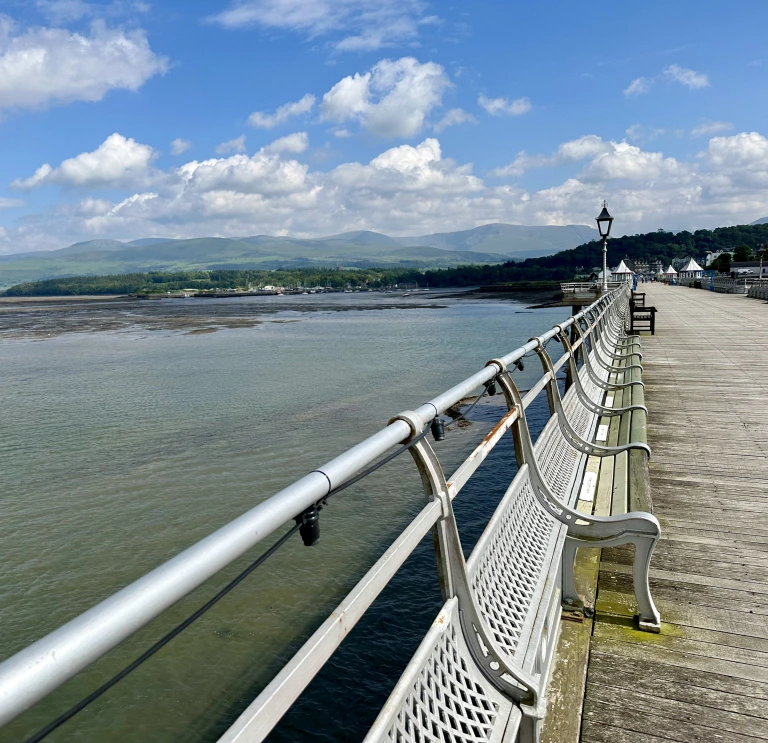 Looking down a long Victorian style pier with the headland and sea in the distance.