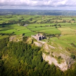 Golygfa o’r awyr o gastell ar fryn yng nghanol caeau gwyrdd.